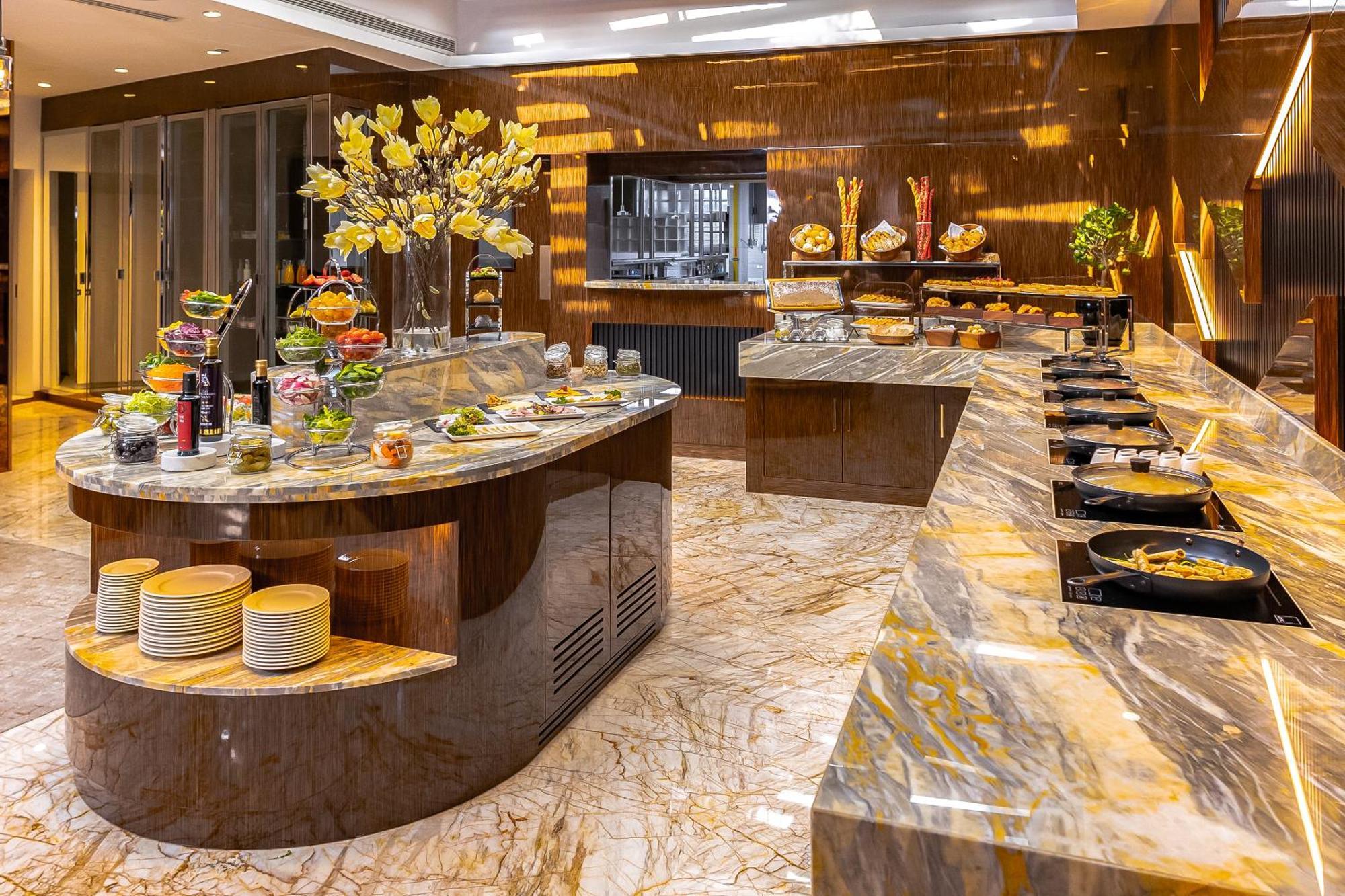 Golden Sands Boutique Hotel-Dubai Creek Εξωτερικό φωτογραφία The photo shows an elegantly designed dining area or buffet setup. There are large, polished marble surfaces with a variety of food items displayed. One main island features a selection of fresh fruits and colorful dishes, surrounded by decorative el
