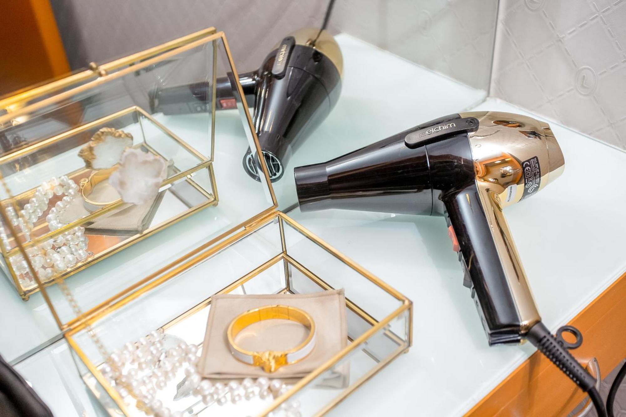 Golden Sands Boutique Hotel-Dubai Creek Εξωτερικό φωτογραφία The photo depicts a stylish bathroom or vanity setup featuring a hairdryer and some jewelry. The hairdryer is predominantly black with gold accents, placed on a light-colored surface. Nearby, there is a glass jewelry box with gold trim, containing va