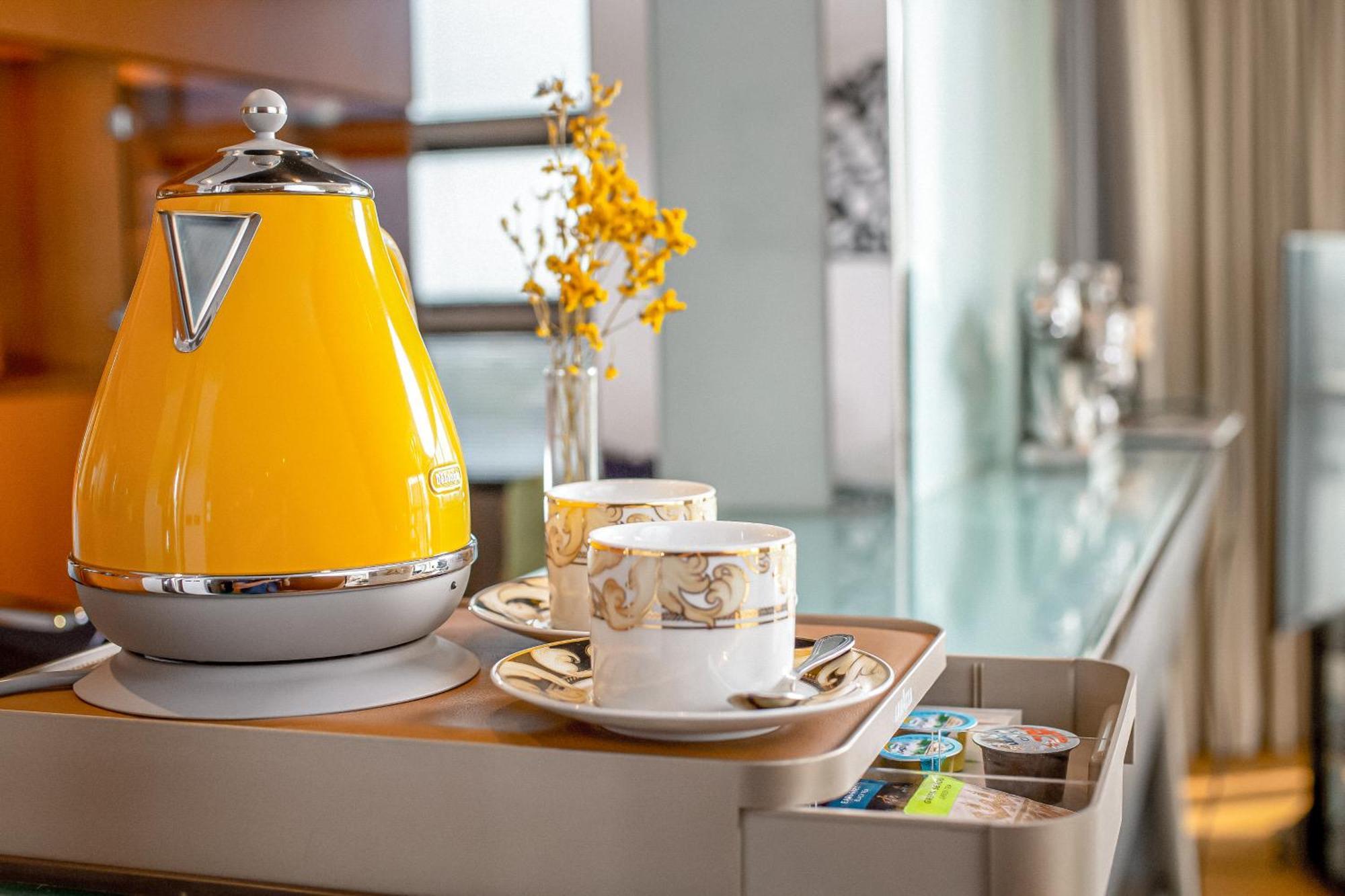 Golden Sands Boutique Hotel-Dubai Creek Εξωτερικό φωτογραφία The photo shows a stylish setup featuring a bright yellow kettle with a chrome accent, placed on a tray. Accompanying the kettle are two elegant tea or coffee cups, each resting on saucers. There is also a small vase containing yellow flowers, adding
