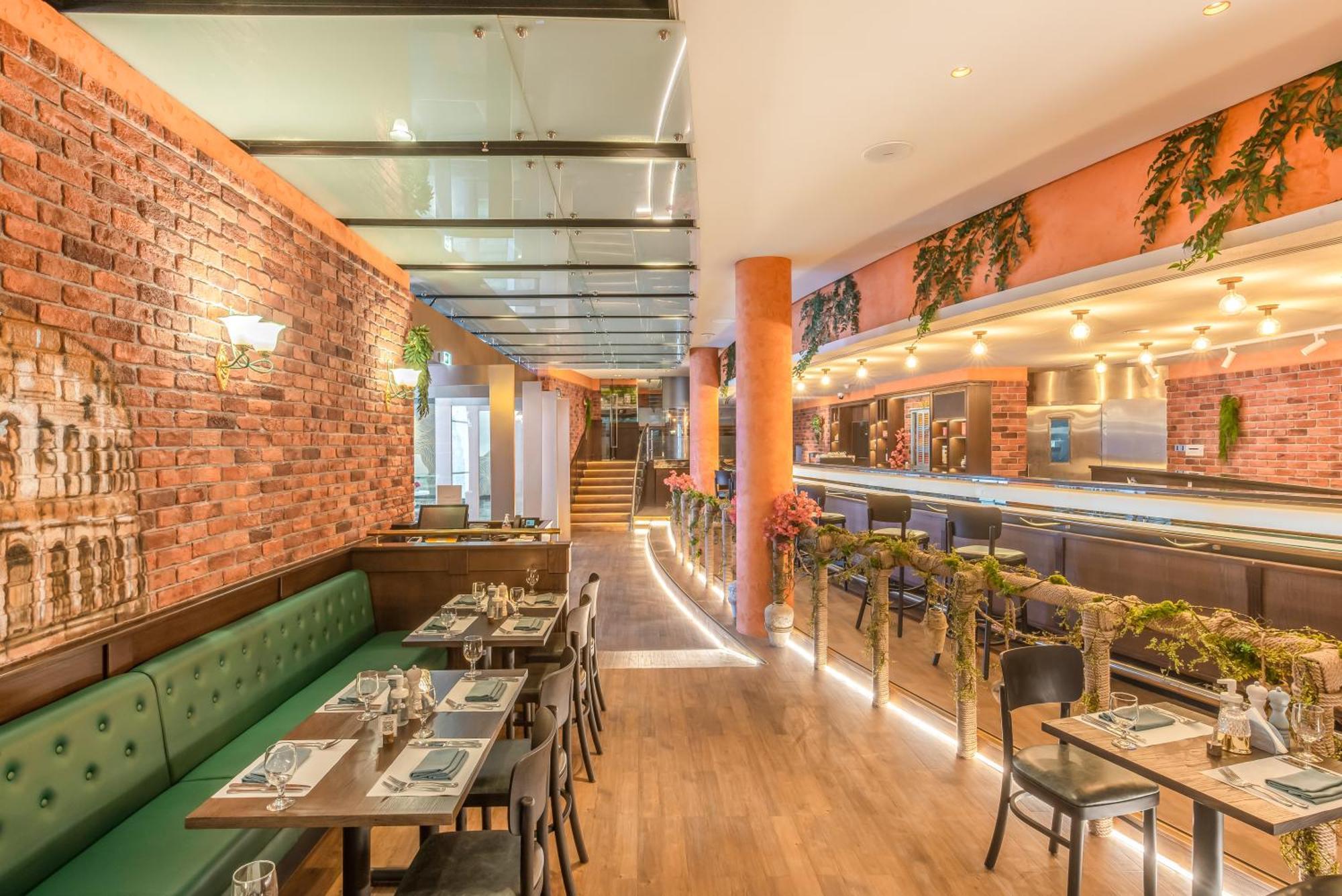 Golden Sands Boutique Hotel-Dubai Creek Εξωτερικό φωτογραφία The photo shows the interior of a modern restaurant featuring a stylish design. The space includes brick walls, large windows, and a glass ceiling that allows natural light to fill the area. There are green upholstered seating areas and neatly arrang