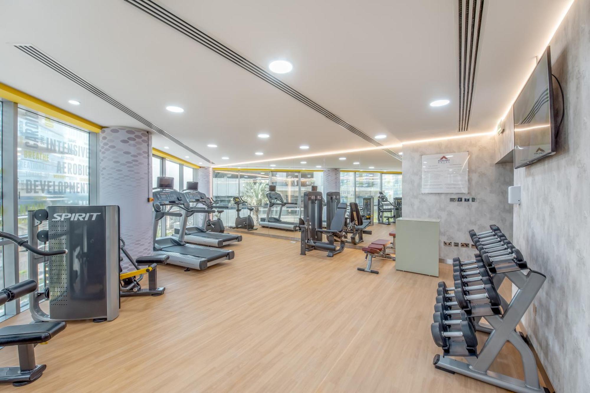 Golden Sands Boutique Hotel-Dubai Creek Εξωτερικό φωτογραφία The image shows a modern gym interior. It features various exercise equipment, including treadmills, weight machines, and free weights. The flooring is a light-colored wood, contributing to a bright and open atmosphere. Large windows allow natural li