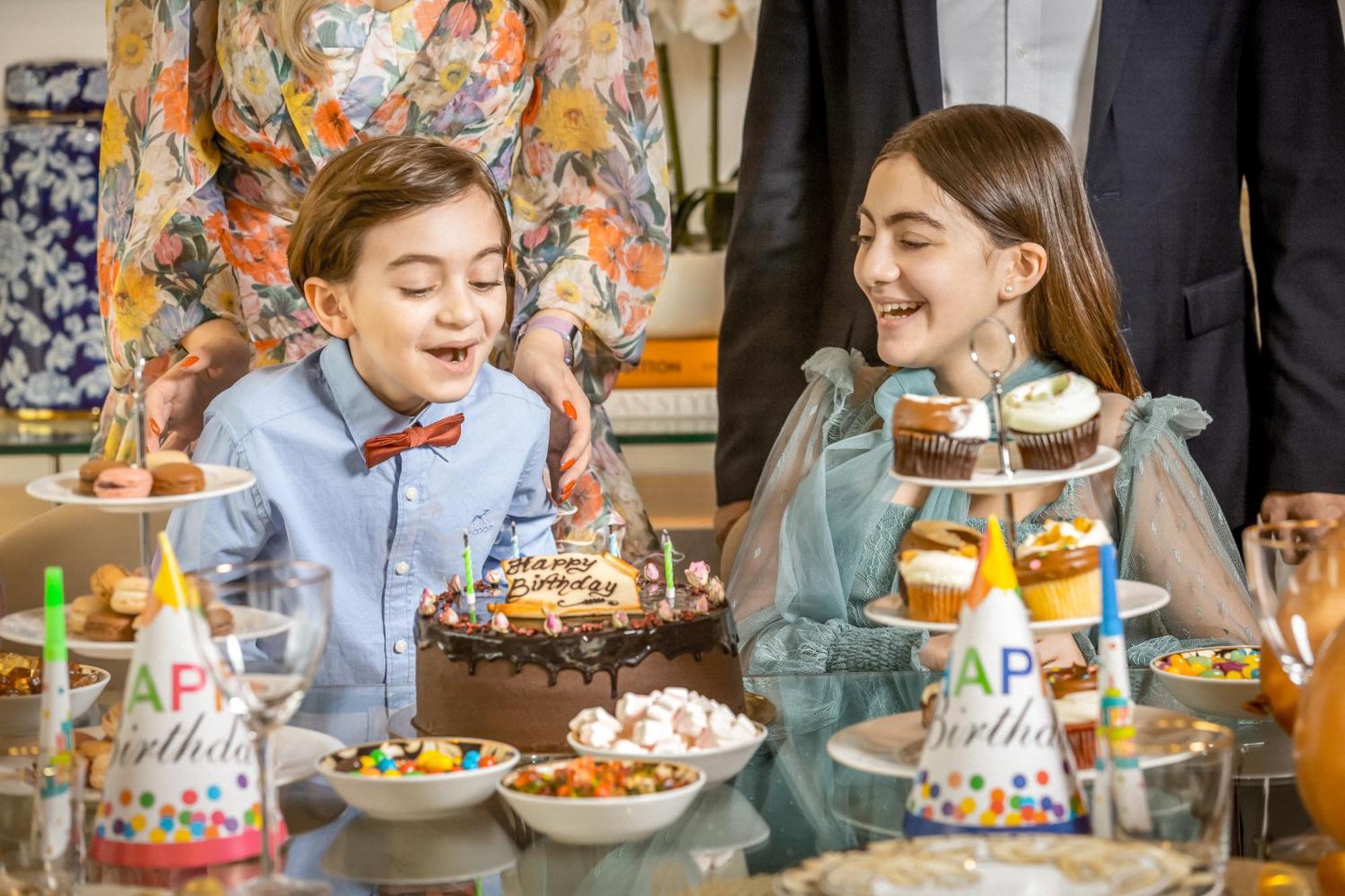 Golden Sands Boutique Hotel-Dubai Creek Εξωτερικό φωτογραφία The photo shows a festive birthday celebration. Two children, a boy and a girl, are smiling and enjoying the moment. The boy, wearing a light blue shirt with a bow tie, sits in front of a chocolate birthday cake that says "Happy Birthday." The girl, 
