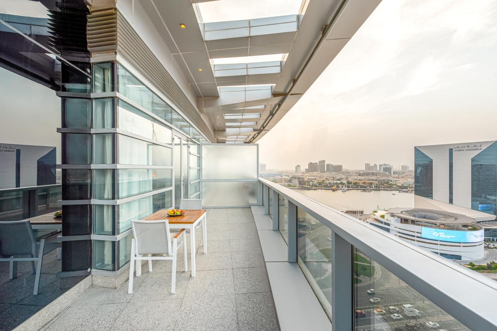 Golden Sands Boutique Hotel-Dubai Creek Εξωτερικό φωτογραφία The photo shows a modern balcony or terrace with a sleek design. It features a glass railing and large windows, providing a clear view of the surroundings. On the balcony, there's a small wooden table with a few items on it, likely for dining or rela