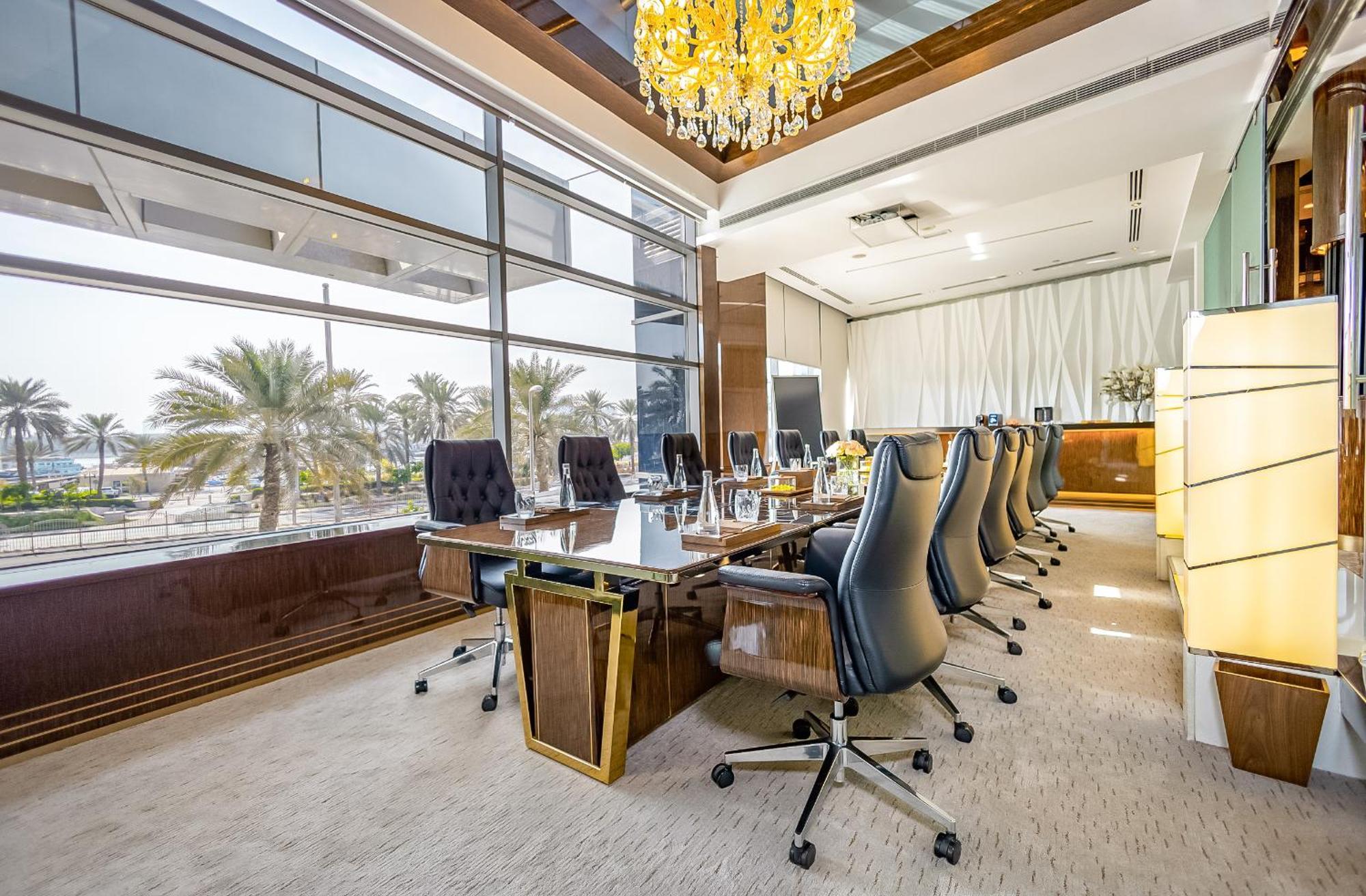 Golden Sands Boutique Hotel-Dubai Creek Εξωτερικό φωτογραφία The photo shows a spacious, modern conference room. It features a long, polished wooden table surrounded by several high-backed chairs. The room has large windows that allow natural light to flood in, offering a view of palm trees outside. A luxuriou