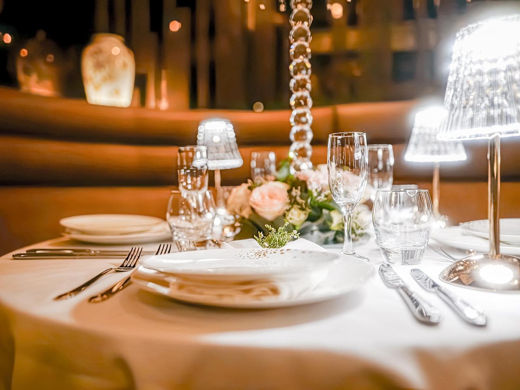 Golden Sands Boutique Hotel-Dubai Creek Εξωτερικό φωτογραφία The photo depicts an elegantly set table in a restaurant, featuring a white tablecloth. The table is adorned with decorative elements, including a floral arrangement with roses and greenery. There are multiple glassware items, such as wine glasses an
