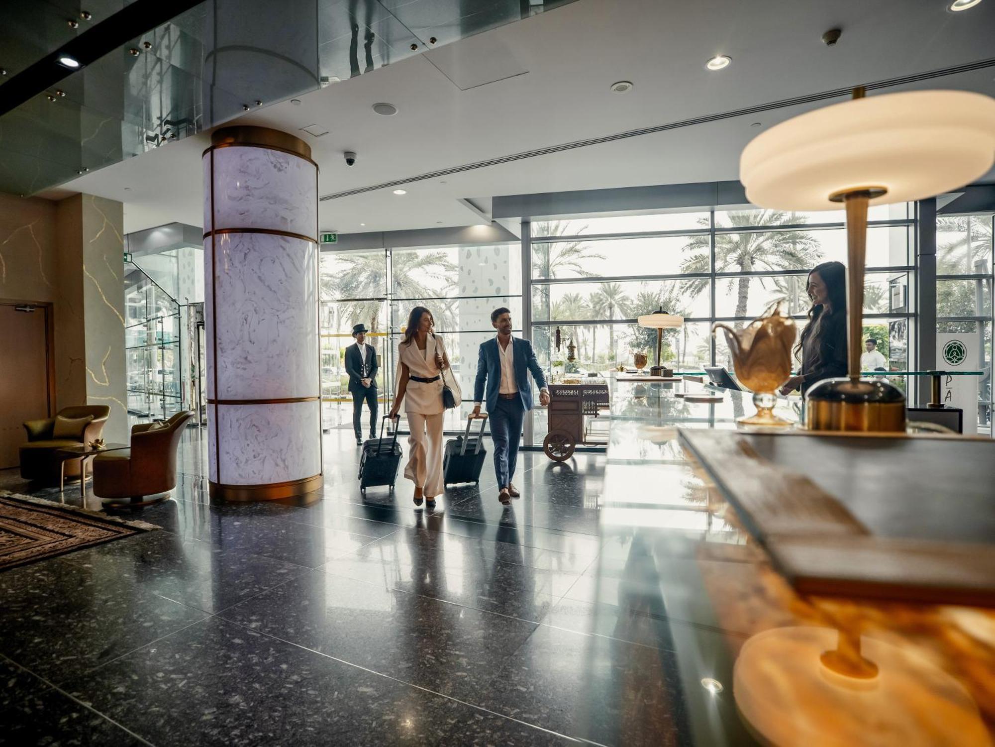 Golden Sands Boutique Hotel-Dubai Creek Εξωτερικό φωτογραφία The photo depicts a modern hotel lobby. There are several people in business attire walking through the space, suggesting they may be arriving or checking in. The lobby features large windows that allow natural light to fill the area, and there are d