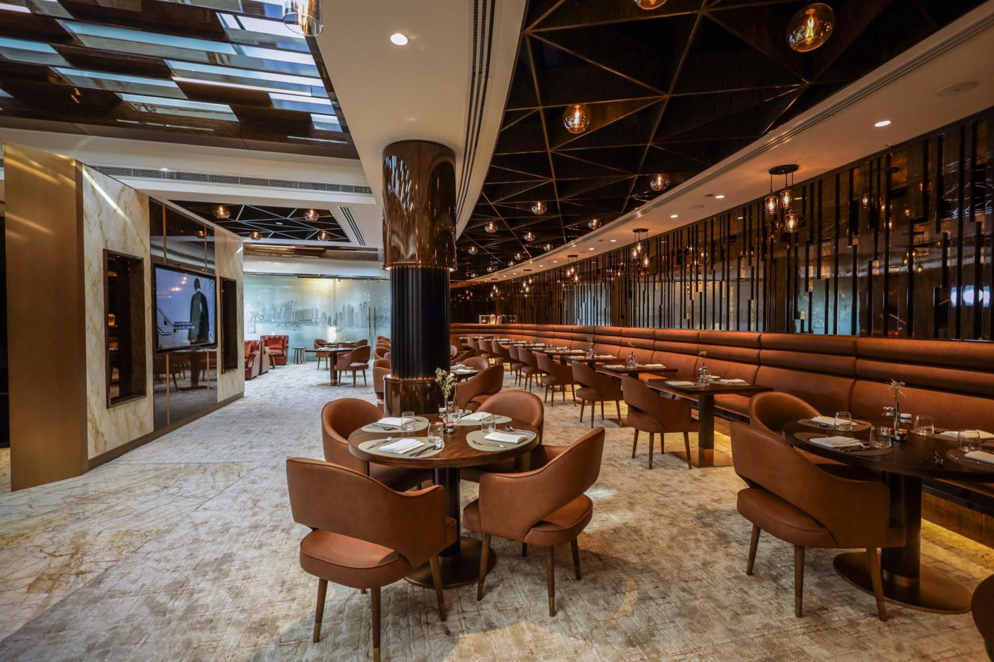Golden Sands Boutique Hotel-Dubai Creek Εξωτερικό φωτογραφία The photo depicts a modern restaurant interior. It features a spacious layout with a mix of seating options, including plush brown chairs and circular tables set for dining. The decor includes elegant lighting fixtures hanging from the ceiling and a 