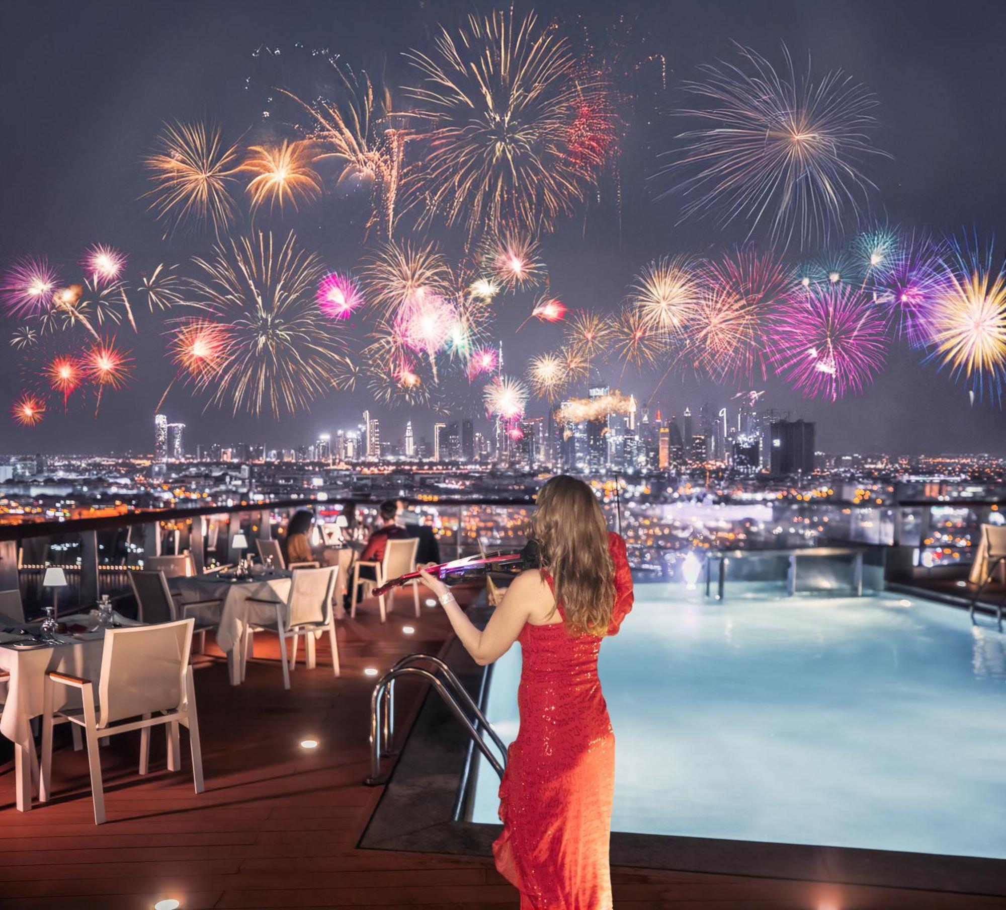 Golden Sands Boutique Hotel-Dubai Creek Εξωτερικό φωτογραφία The photo depicts a rooftop setting with a swimming pool, where a woman in a elegant red dress stands, gazing at a stunning fireworks display lighting up the night sky. The background showcases a city skyline, sparkling with lights and buildings, whi
